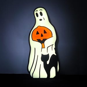May include: A white ghost holding a carved orange pumpkin with a black cat peeking out from behind the ghost.