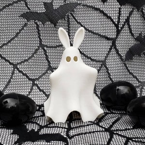 May include: A white ghost bunny figurine with black eyes and a black spiderweb background. There are four black eggs around the bunny.