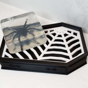 Op de afbeelding: Een zwart-witte spinnenweb zeepbakje met een doorzichtige zeep met een zwarte spin erin.