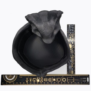 Puede incluir: Maceta de cer&aacute;mica negra con forma de cabeza de serpiente con una abertura redonda y ancha. La maceta tiene un di&aacute;metro de aproximadamente 15 cm.