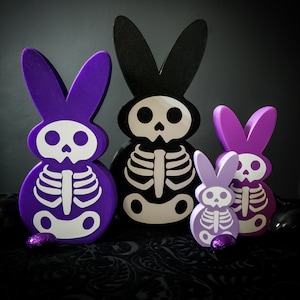 May include: Four purple and white skeleton bunny figurines. The bunnies are in different sizes and have a skull and crossbones design.