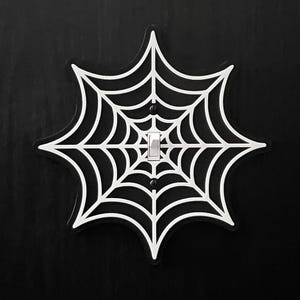 Könnte beinhalten: Ein weißer Lichtschalter-Abdeckung aus Kunststoff in Form eines Spinnennetzes. Der Schalter ist ausgeschaltet.