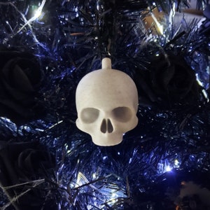 May include: White skull-shaped Christmas bauble hanging on a black tinsel Christmas tree.