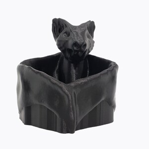 Puede incluir: Un macetero en forma de murci&eacute;lago de color negro impreso en 3D con una cabeza de murci&eacute;lago detallada que sobresale de la parte superior.