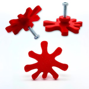 May include: Red, splash-shaped cabinet knobs with silver screws. These unique knobs have an abstract design, ideal for adding colour and personality to furniture. Knobs are shown from multiple angles.