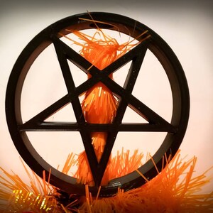 An inverted black pentagram in a circle mounted on top of an orange tree. The tree is going through the centre of the tree topper and can be seen within the empty spaces between the star.