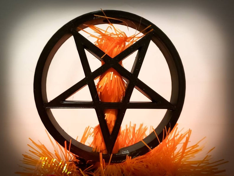 An inverted black pentagram in a circle mounted on top of an orange tree. The tree is going through the centre of the tree topper and can be seen within the empty spaces between the star.