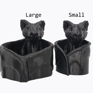 Puede incluir: Dos macetas en forma de murci&eacute;lago impresas en 3D de color negro, una etiquetada como "Grande" y la otra como "Peque&ntilde;a".
