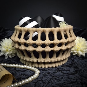 May include: A beige bone-shaped basket holds black and white striped and solid black eggs. The basket is decorated with white flowers and a pearl necklace. The background is dark.