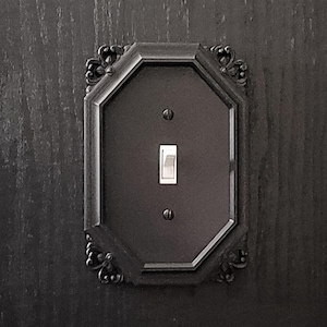 May include: A black octagonal light switch plate with ornate detailing and a white toggle switch.