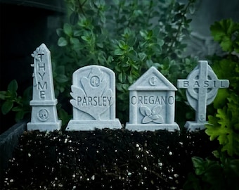 Puede incluir: Cuatro marcadores de jardín de piedra gris claro con forma de lápidas en miniatura. Los marcadores están etiquetados con las palabras THYME, PARSLEY, OREGANO y BASIL, cada uno con un pequeño icono en relieve de la planta o calavera.