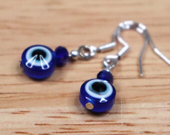 May include: A pair of silver earrings with blue evil eye charms. The charms are round and have a white center with a blue eye.
