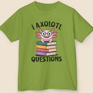 May include: Green t-shirt featuring a cartoon axolotl wearing glasses and sitting on a stack of books. The text "I axolotl questions" is printed above and below the axolotl illustration. The shirt is made of a soft material.
