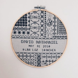 Könnte beinhalten: Ein schwarz-weißer Stickrahmen mit geometrischem Muster. Der Rahmen enthält den Text "DAVID NATHANIEL", "MAY 31 2019", "9 LBS 1 OZ" und "19 INCHES".