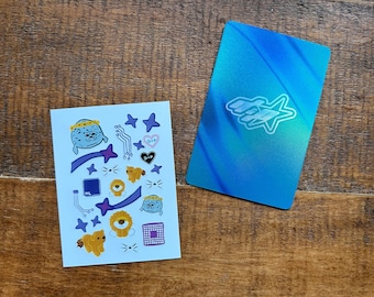 May include: A light blue sticker sheet featuring various illustrations including two round blue creatures with crowns, two yellow lions, purple shooting stars, circuit board lines, and hearts with the text D+P, alongside a blue metallic rectangular card.