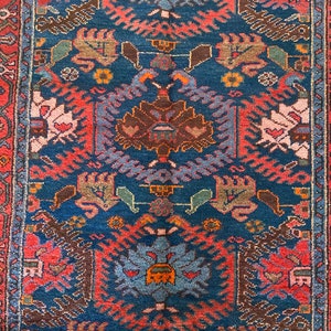 May include: A vintage rug with a blue background and intricate patterns in shades of red, brown, and green. The rug features a central medallion with a floral design and repeating geometric motifs.