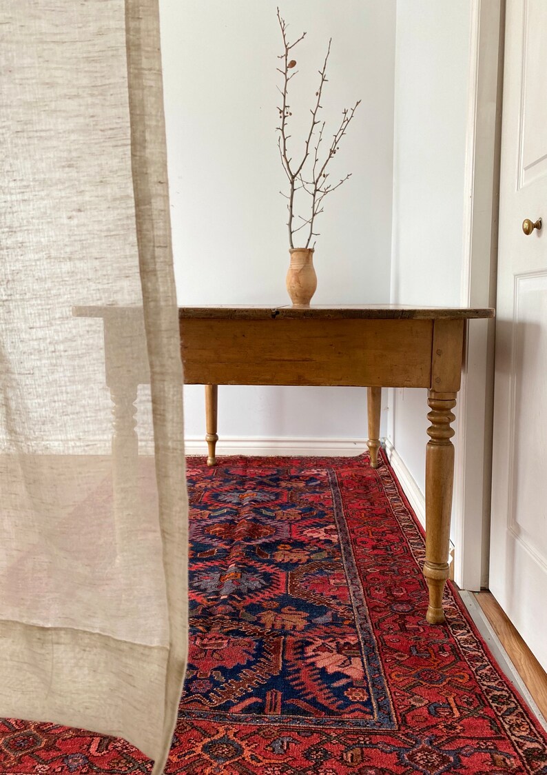 May include: A wooden table with turned legs sits on a red and blue patterned rug. A vase with dried branches sits on the table.
