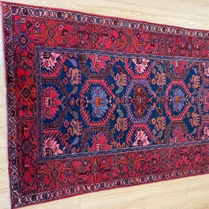 May include: A traditional Persian rug with a deep blue center and a red border. The rug features intricate floral and geometric patterns in shades of pink, red, blue, and purple.