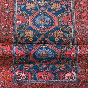 May include: A vintage Persian rug with a deep blue background and intricate red, brown, and white patterns. The rug has a fringed edge and is woven with a traditional design.