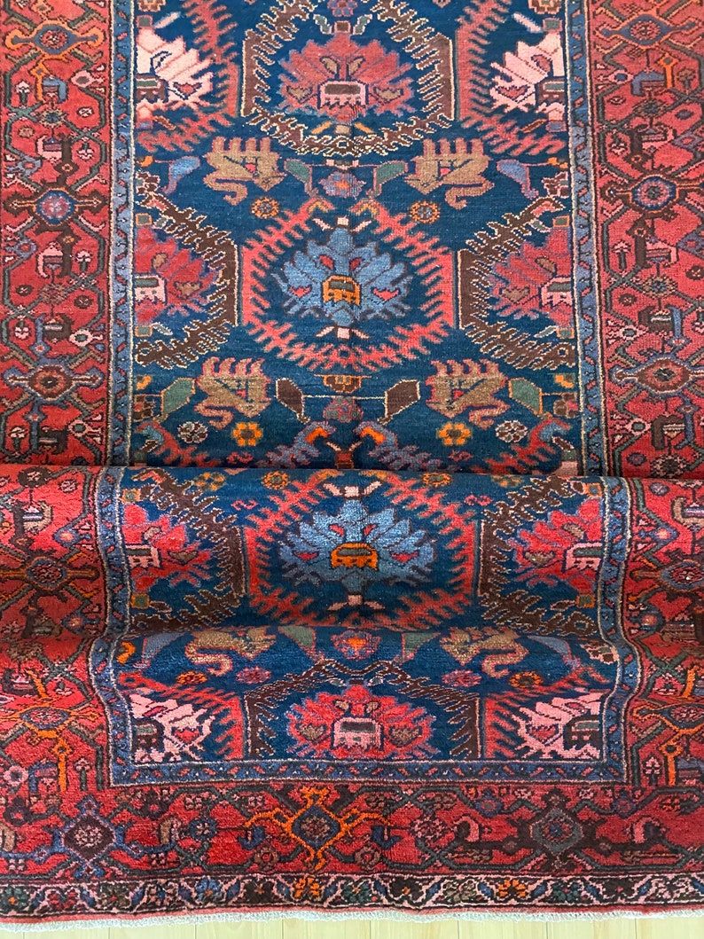 May include: A vintage Persian rug with a deep blue background and intricate red, brown, and white patterns. The rug has a fringed edge and is woven with a traditional design.