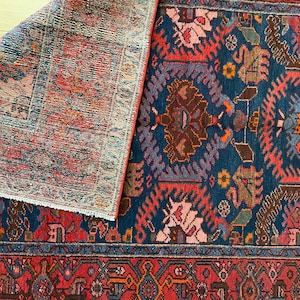 May include: A vintage rug with a blue background and intricate red, pink, and brown floral patterns. The rug has a fringe border and is folded in half.