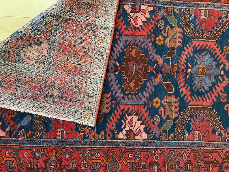 May include: A vintage rug with a blue background and intricate red, pink, and brown floral patterns. The rug has a fringe border and is folded in half.