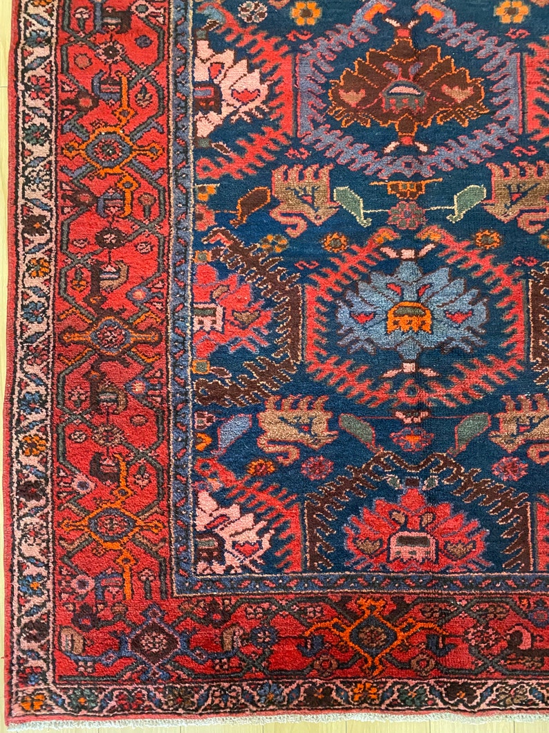 May include: A vintage Persian rug with a deep blue center and a red border. The rug features intricate floral and geometric patterns in shades of red, blue, brown, and beige.