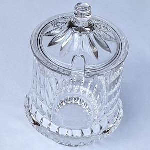 Könnte beinhalten: Eine klare Glasschüssel mit Deckel. Die Schüssel hat ein dekoratives, geschliffenes Glasdesign.