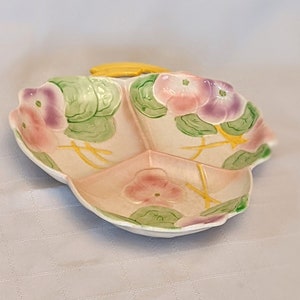 Op de afbeelding: Een verdeelde serveerschaal met een bloemenmotief. De schaal is wit met roze, paarse en groene bloemen. De schaal heeft een gele handgreep.