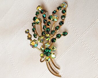 May include: A gold-toned brooch with a floral design featuring green and clear rhinestones.