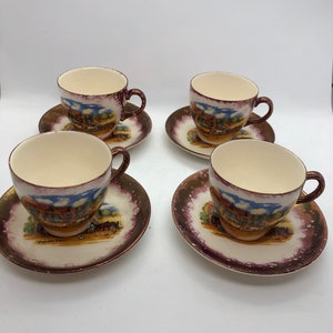 May include: Set of four vintage teacups and saucers with a colourful floral design and gold accents. Each cup and saucer features a different scene of a building with a thatched roof and a horse-drawn carriage.