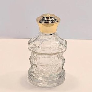 May include: A clear glass bottle with a gold lid. The bottle has a textured design and is approximately 10 cm tall.