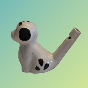 May include: A white ceramic whistle shaped like a Dalmatian dog with black spots. The whistle has a black and white spotted design and a black nose.