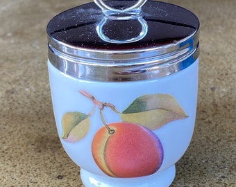 May include: White ceramic egg cup with a silver lid and handle. The egg cup has a peach design with green leaves.