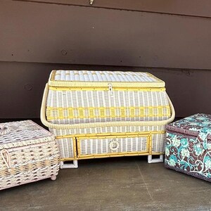 May include: Three vintage wicker sewing boxes. One is white with yellow accents and a drawer. Another is white with pink accents. The third is brown with a floral pattern.