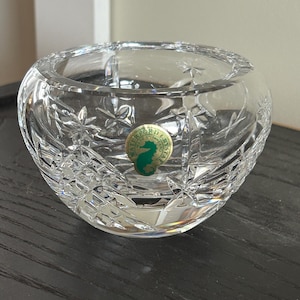 May include: A clear glass bowl with a cut crystal design. The bowl has a round shape and a small, round sticker on the bottom that says "Waterford Crystal".