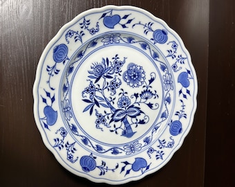 Op de afbeelding: Een wit keramiek bord met een blauw en wit bloemenmotief. Het bord heeft een gegolfde rand en een verhoogde rand.