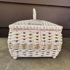 May include: A woven wicker basket with a pink lid and a woven handle. The basket has a white and brown pattern.