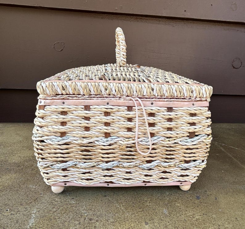 May include: A woven wicker basket with a pink lid and a woven handle. The basket has a white and brown pattern.