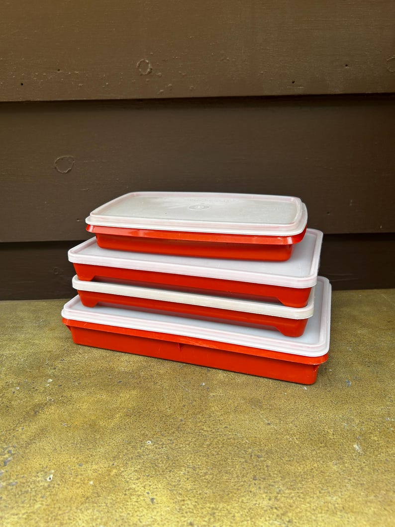Op de afbeelding: Een stapel van drie rechthoekige opbergbakjes met feloranje onderkanten en doorschijnende witte deksels. De bakjes zijn verticaal op elkaar gestapeld en hebben elk een plat ontwerp met afgeronde hoeken en een goed sluitend deksel.