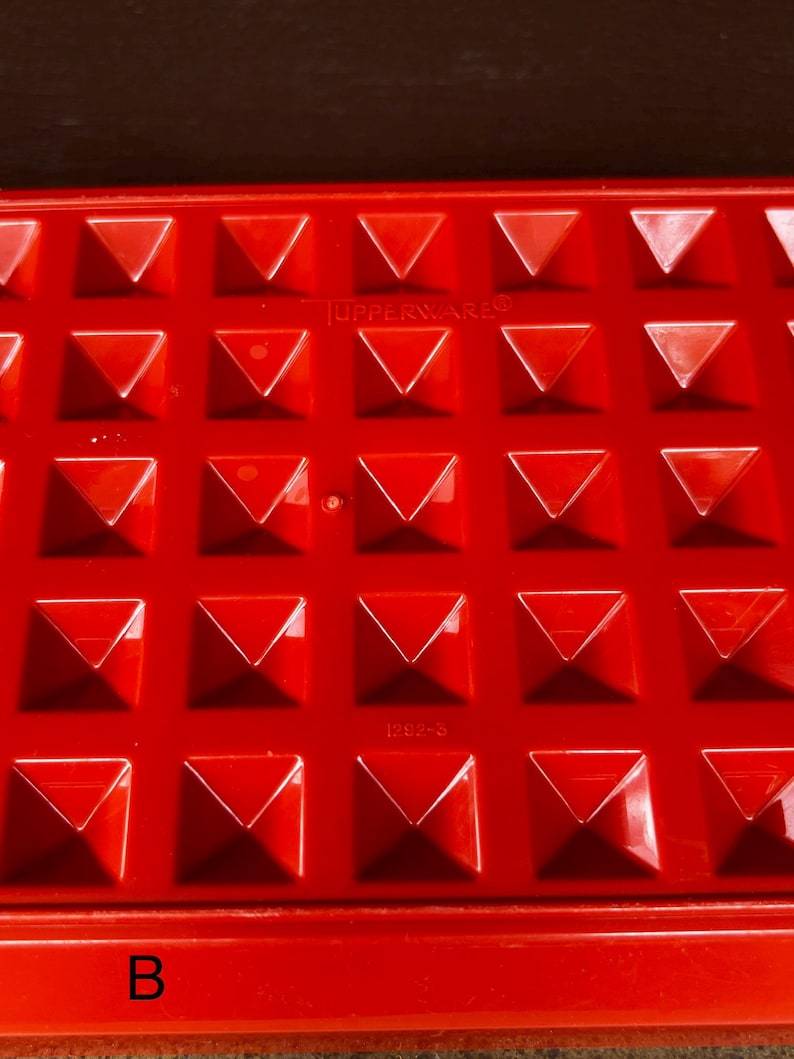 Op de afbeelding: Een felrood plastic Tupperware-dienblad met een herhalend raster van verhoogde, piramidevormige inkepingen. Het oppervlak bevat de in reli&euml;f aangebrachte tekst TUPPERWARE en het nummer 1292-3, met een grote zwarte letter B linksonder.