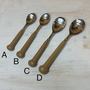 Puede incluir: Cuatro cucharas vintage con un cuenco plateado brillante y un mango marrón claro. Los mangos tienen un extremo redondeado y un anillo decorativo cerca del cuenco. Las cucharas están dispuestas en fila sobre una superficie clara.
