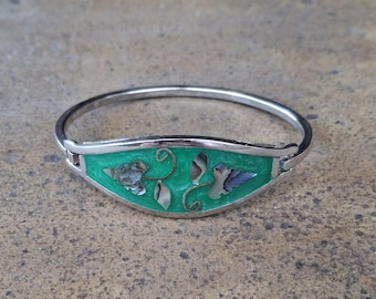 May include: Silver-tone bangle bracelet with a vibrant green enamel center. The enamel is adorned with shell and leaf designs. The bracelet is a hinged style, and the overall design is elegant and eye-catching.