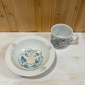 Peut inclure: Un bol et une tasse en céramique blanche avec un motif Cabbage Patch Kid. Le bol et la tasse présentent une image de dessin animé d'un bébé Cabbage Patch Kid dans un chou.