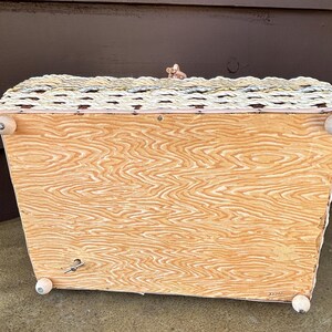 May include: A vintage wicker music box with a white painted base and wooden feet. The music box has a woven design and a small crank on the side.