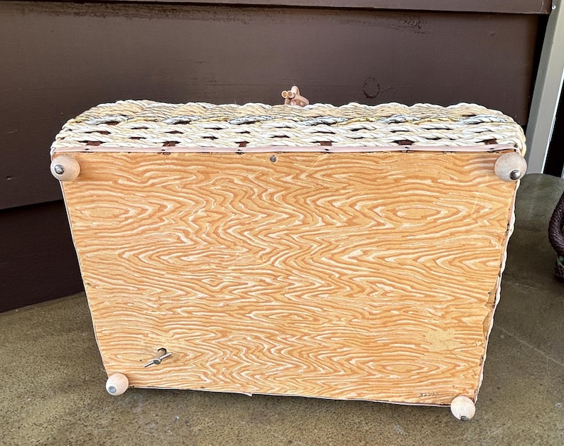 May include: A vintage wicker music box with a white painted base and wooden feet. The music box has a woven design and a small crank on the side.
