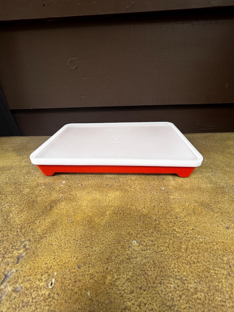 Op de afbeelding: Een rechthoekige opbergcontainer met een felrode basis en een doorschijnend wit deksel. Het deksel is voorzien van een gecentreerd rond logo en een opstaande rand, terwijl de basis een platte bodem en rechte zijkanten heeft voor een eenvoudig ontwerp.
