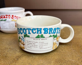 Puede incluir: Taza de sopa de cerámica blanca con una ilustración azul y verde de verduras y el texto "Scotch Broth" y una receta de Scotch Broth. La receta incluye 1 lb de cuello de cordero, 2 puerros, 1 cucharadita de sal, 1 litro de agua fría, 1 nabo pequeño, 1 tallo de apio, pimienta, 1 1/2 oz de cebada perlada y 1 cucharadita de perejil.