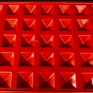 Op de afbeelding: Een felrode rechthoekige plastic vorm met een raster van verhoogde piramidevormige inkepingen. Het oppervlak toont de in reli&euml;f aangebrachte tekst TUPPERWARE en het nummer 1292-4. Een grote letter A staat in de linkerbenedenhoek.