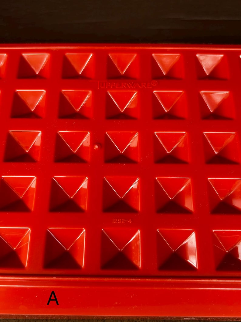 Op de afbeelding: Een felrode rechthoekige plastic vorm met een raster van verhoogde piramidevormige inkepingen. Het oppervlak toont de in reli&euml;f aangebrachte tekst TUPPERWARE en het nummer 1292-4. Een grote letter A staat in de linkerbenedenhoek.
